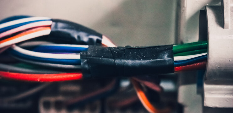 Multicolored electrical wires bundled and secured with black tape, inserted into metal connector, close-up view.
