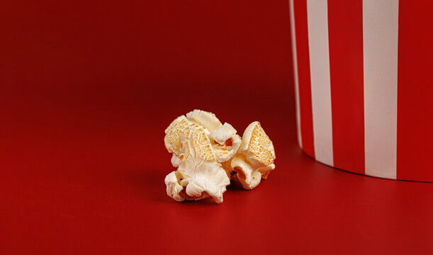 Horizontal shot of popcorn kernels and striped cup border on red. Minimalist food background.