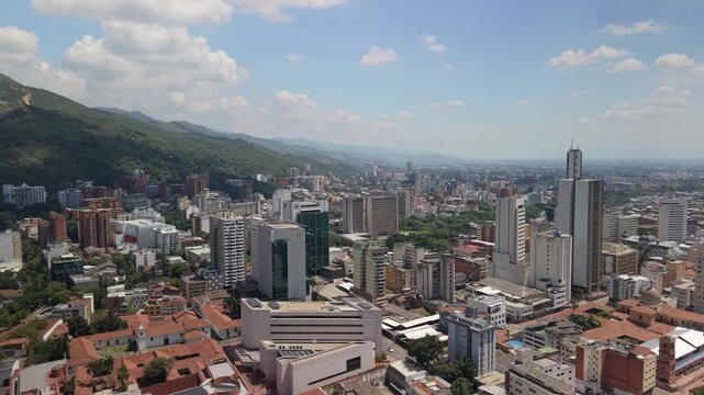 Drone orbit sequence revealing the lush Farallones mountains and downtown skyline of Cali. View includes colonial rooftops, modern office buildings, and the iconic Torre de Cali tower.