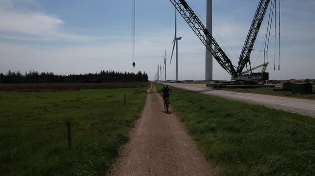 Cyclist riding near wind turbines construction site, renewable energy and sustainable lifestyle concept
