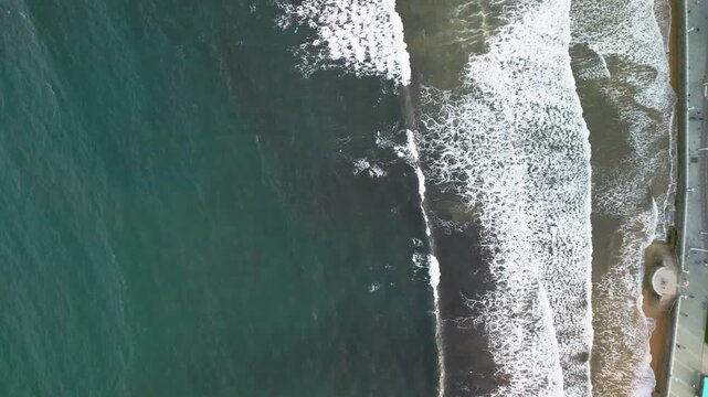 Gijon Spain aerial drone top down view of stormy ocean waves and white foam texture.
