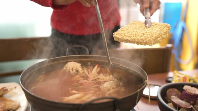 Chef putting classic Korean noodle or Ramyon into spicy and sour seafood soup