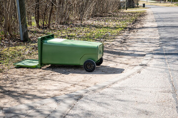 Green Garbage Bin Lying on Side Near Roadside with Open Lid Outdoors