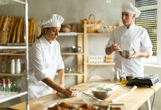 Mature man chef and woman kneading and shaping dough to make bread, croissants and baguettes