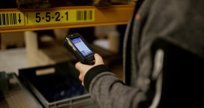 vClose-up of warehouse worker hand holding handheld mobile terminal with screen in distribution center