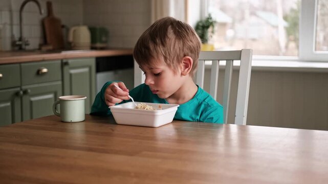 6 years old boy eats instant noodle from box. Child is eating Asian ramen. Lunch time. A good appetite. Tasty children food. Close-up portrait. Carbs dinner. Fast food. Kid eating by himself with fork