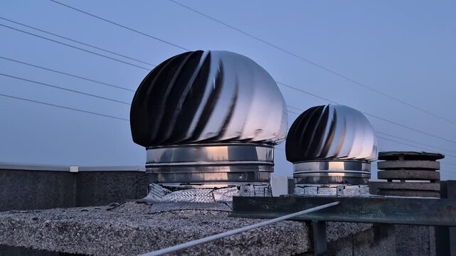 Rooftop terrace concrete floor with stainless steel vent caps and chimney pots in motion, filmed outdoors at sunset on a modern building.