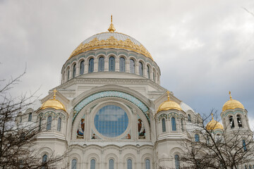 Fototapeta premium Majestic white Orthodox cathedral with ornate golden domes under a cloudy sky. Naval Cathedral of St. Nicholas in Kronstadt.
