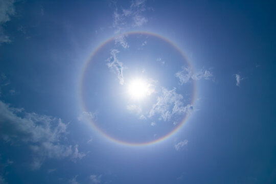 Sun halo effect in clear blue sky with light clouds.