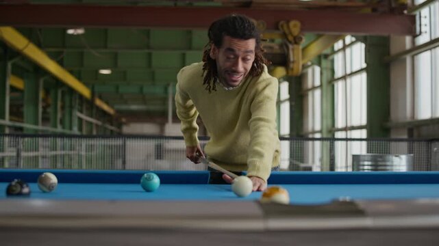 Tracking medium shot of young Biracial man aiming with cue, making precise shot on billiard table and giving high five to friend during exciting indoor game