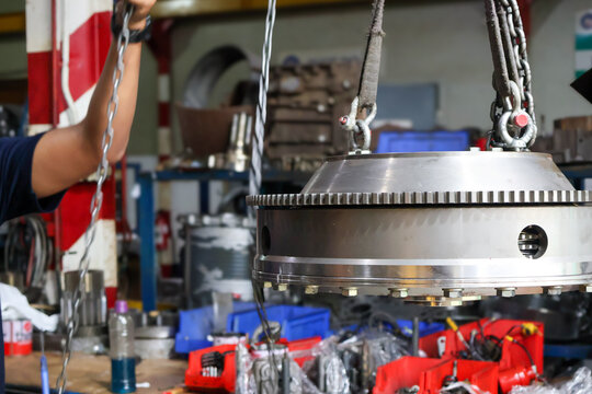 Close up of a heavy steel flywheel being lifted by a chain hoist