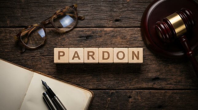 Wooden cubes spelling the word PARDON rest on a rustic wooden surface alongside eyeglasses a gavel and an open notebook with a pen justice legal law concept decision freedom