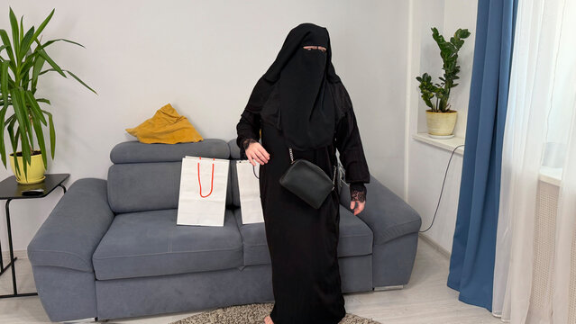 Adult Muslim woman in abaya holding shopping bag in bright interior. Concept of modest fashion and lifestyle.