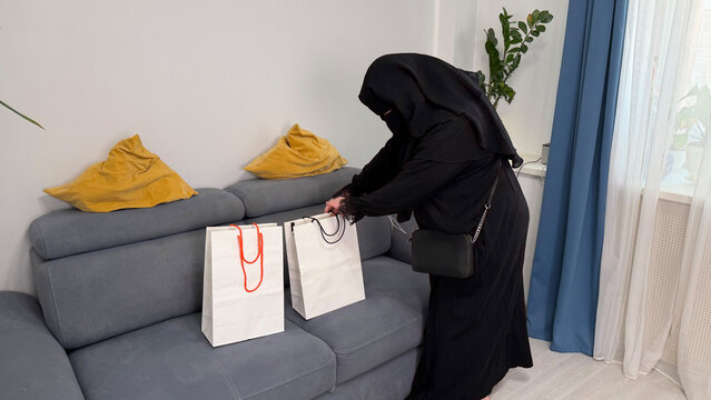 Muslim woman placing shopping bag on sofa at home