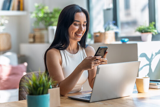 Beautiful woman using smartphone while working with laptop in the livingroom at home
