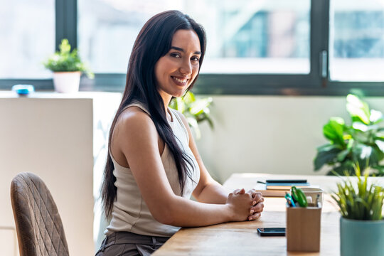 Beautiful woman looking at camera while working with laptop in the livingroom at home