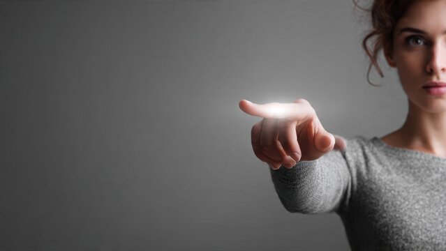 Woman's glowing finger ready to interact with a futuristic digital interface. A conceptual image representing innovation, technology, and virtual touch on a grey background.