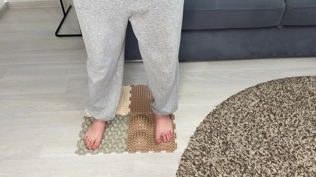 Close up of female feet walking on orthopedic massage mat. Person does foot exercises for flat feet prevention and sensory stimulation. Health care, wellness and relaxation concept at home