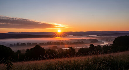 Fototapeta premium Serene sunrise over a misty valley with a winding river and lush greenery in a peaceful natural landscape at dawn