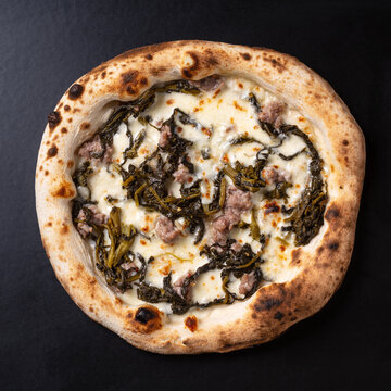 Pizza Salsiccia e Broccoli Rabe, a typical Neapolitan specialty. Photographed against a black background.