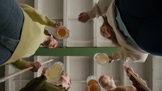 Bottom view shot of four multiethnic friends toasting with mugs of beer and chatting while standing with billiards cues in indoor setting, showing relaxed social interaction and fun