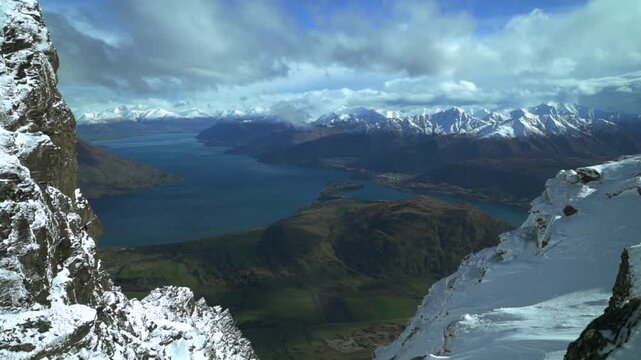 The Remarkables Ski Resort top of jagged snowy covered peaks Rock face cold winter morning sunny blue sky clouds New Zealand Lake Wakatipu lush green valley blowing wind snow slide left motion