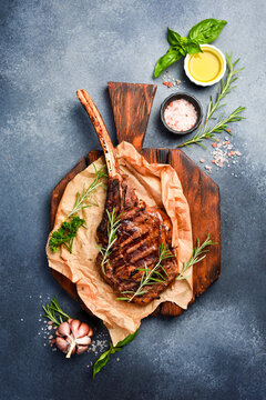 Beef steak on the bone. Grilled tomahawk steak with rosemary and spices on a cutting board. Top view. Free space for text.
