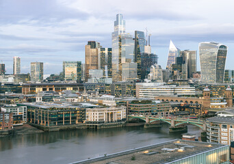 Obraz premium The City of London skyline showcases a striking blend of historic architecture and modern, glass-clad skyscrapers under soft, overcast sky.In the foreground, the calm River Thames reflects the urban l
