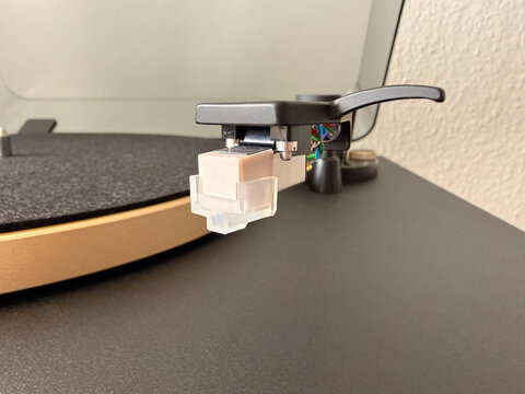 Detailed close-up of a modern turntable cartridge and stylus with a protective plastic cover. High-quality analog audio equipment showing the tonearm and headshell on a minimalist background.