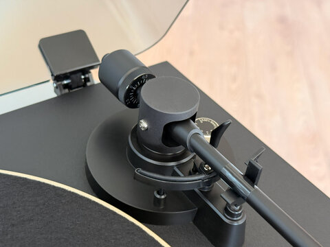 Top view close-up of a modern matte black turntable tonearm assembly, showcasing the counterweight and precision tracking force adjustments. High-quality analog audio gear for music enthusiasts.
