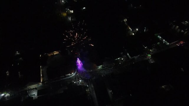 Aerial view of packaged fireworks exploding over a residential neighborhood at night in 4K resolution.