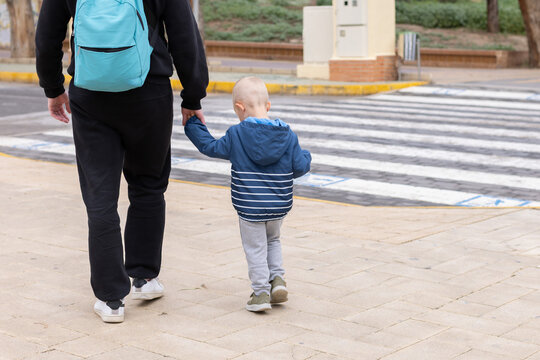 Father with his little son walks towards the zebra crossing. Back view.