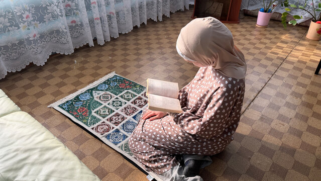 Saudi Arabia woman reading Quran on prayer rug during Ramadan