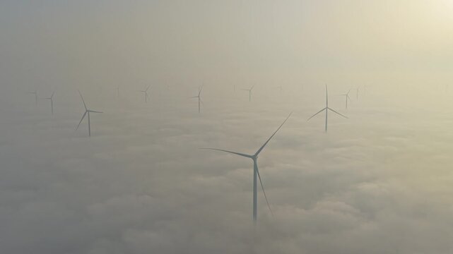 Aerial view of an offshore wind farm with turbines spinning above a thick layer of fog. Clean and sustainable energy production