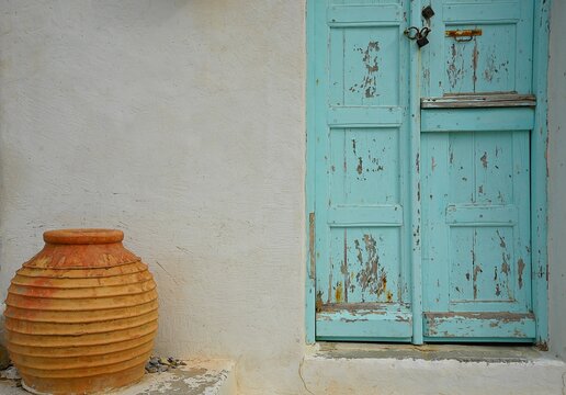 Old traditioal rural house facade with a weathered turquoise wooden door and a handmade terracotta unglazed urn in Amorgos island, Cyclades Greece.