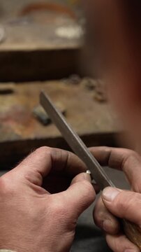 Jeweler crafting ornate silver crown with fleur-de-lis motif and detailed patterns in workshop. Traditional jewelry making process in workshop environment
