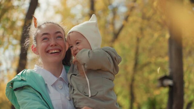 Bright grove white caregiver holds baby close, playful nibble and shared laughter, protective embrace, candid portrait, sunlight filtering through trees, tender interaction, warm family feeling