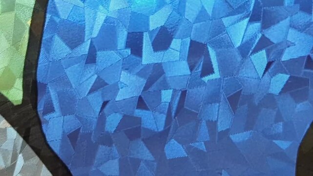 A high-quality, abstract close-up shot of a decorative stained glass window. The footage showcases intricate geometric patterns and a rich palette of colors including green, blue, purple, and amber. 