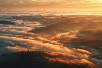 Obraz premium Golden Hour Aerial View of Misty Mountains and Rolling Hills Bathed in Warm Sunlight with a Soft Orange Sky Above