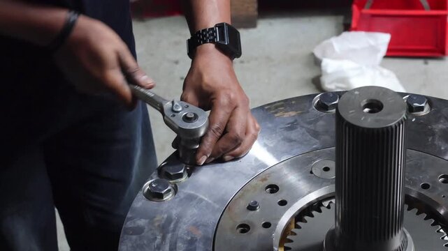 ​A technician uses a large manual ratchet wrench to tighten heavy-duty bolts on an industrial transmission assembly featuring a splined shaft.