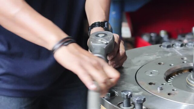​A professional mechanic uses a heavy-duty large ratchet tool to tighten bolts on a massive industrial gearbox component during assembly.