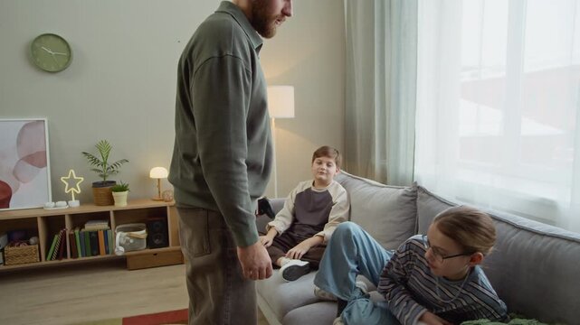 Long handheld shot of adult Caucasian father taking joysticks away from his children while limiting playing time at home