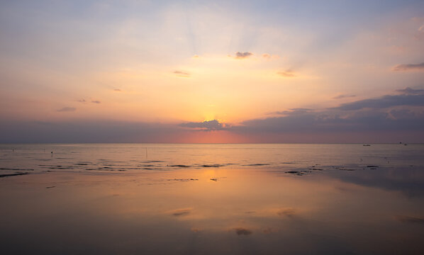 Serene sunset over the ocean with sun rays and water reflection.
