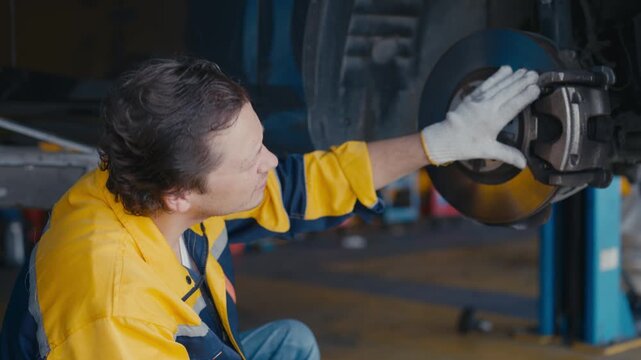Mechanic brake rotor car repair worker glove wheel garage service vehicle repair technician inspecting brake system garage workshop with lifted car and tool tablet mechanic inspecting brake disc