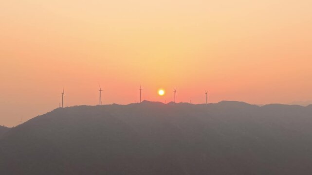 Documentary Aerial: Red Sunrise Over Mountain Ridge with Row of Spinning Wind Turbines