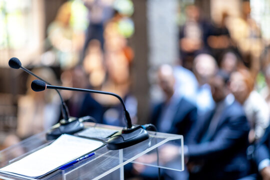 Microphones in focus at business conference, corporate presentation, workshop, coaching training, news conference, company meeting, public or political event. Public speaking concept.