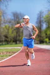 Obraz premium Elderly man running on a track and checking his smartwatch