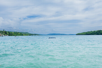 small floating fish farm platform on the calm turquoise sea with a lush green island background © anwar