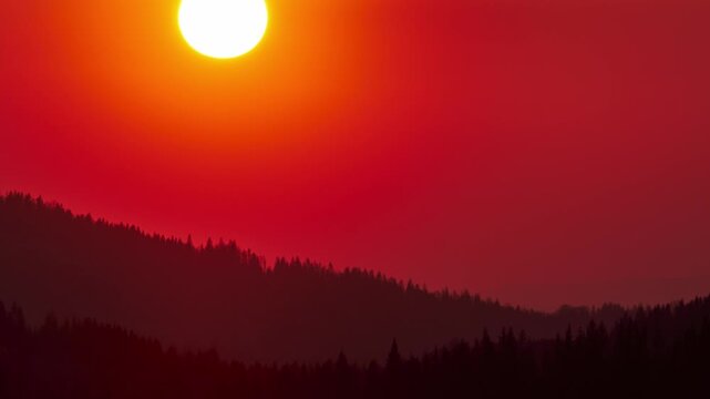 Cinematic time lapse of vibrant red sunset over mountain forest silhouette