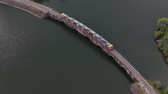 Aerial view of a train crossing a stone bridge over the dark water, connecting land masses with green vegetation, Mesao Frio, Portugal.